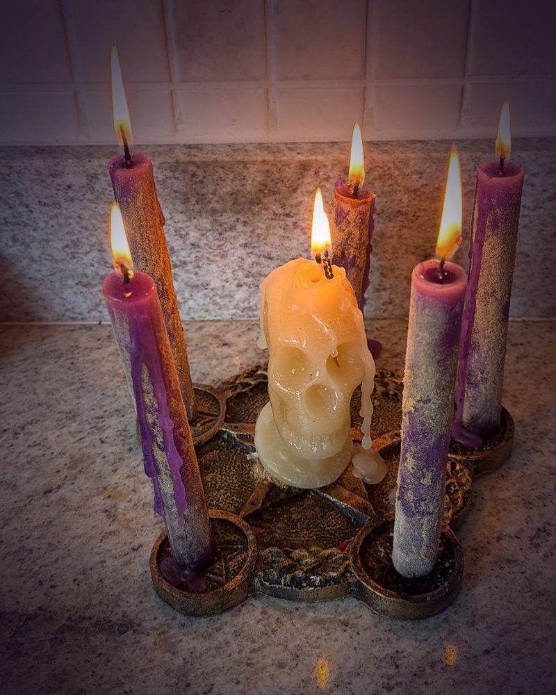 Velas roxas acesas em um castiçal de pentagrama, com uma vela de caveira ao centro, no altar da Bruxa Évelyn
