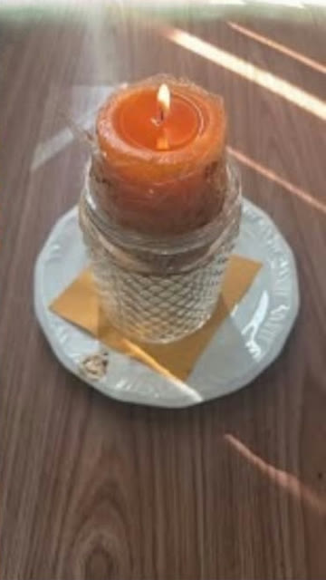 Vela laranja acesa em um copo de cristal sobre um pires, com papel dobrado embaixo